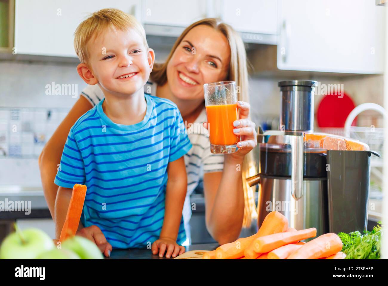 Mom and son drink fresh carrot juice squeezed using juicer in kitchen at home Stock Photo