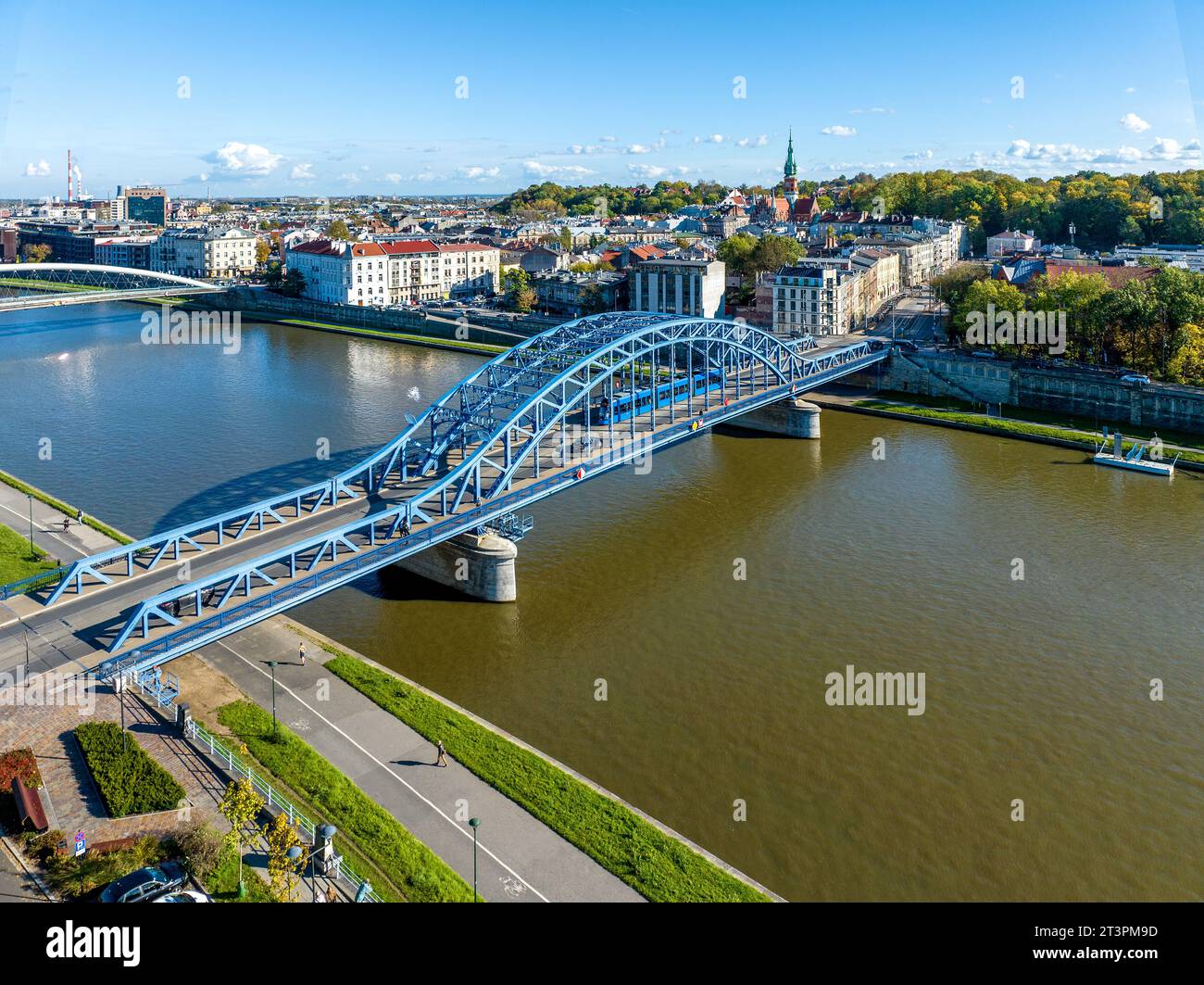 Krakow, Poland. Pilsudski blue tied arc bridge over Vistula River with tramway,  blue tram, sidewalk and bicycle lane. Boulevards on riverbanks. Podgo Stock Photo