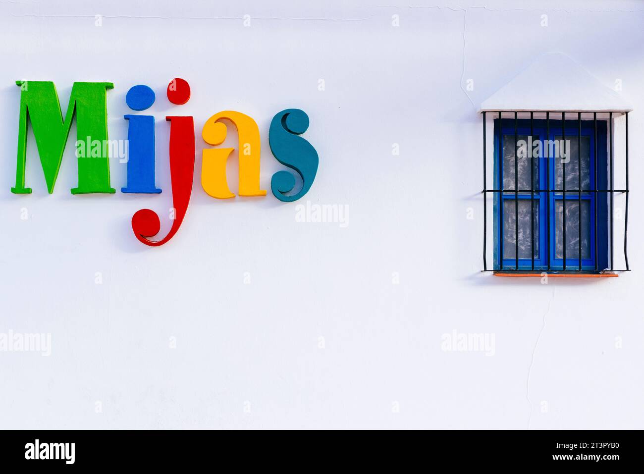 White wall with blue window and the multicolored Mijas logo. Mijas