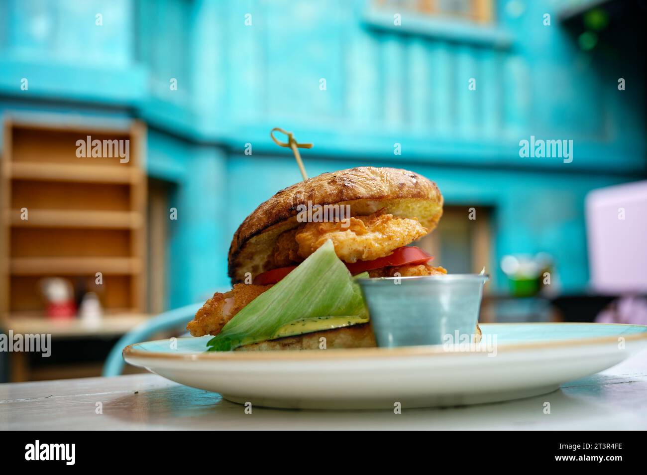Stacked chicken hamburger, enjoyed in a chic restaurant nestled in an open courtyard with vivid blue walls. Stock Photo