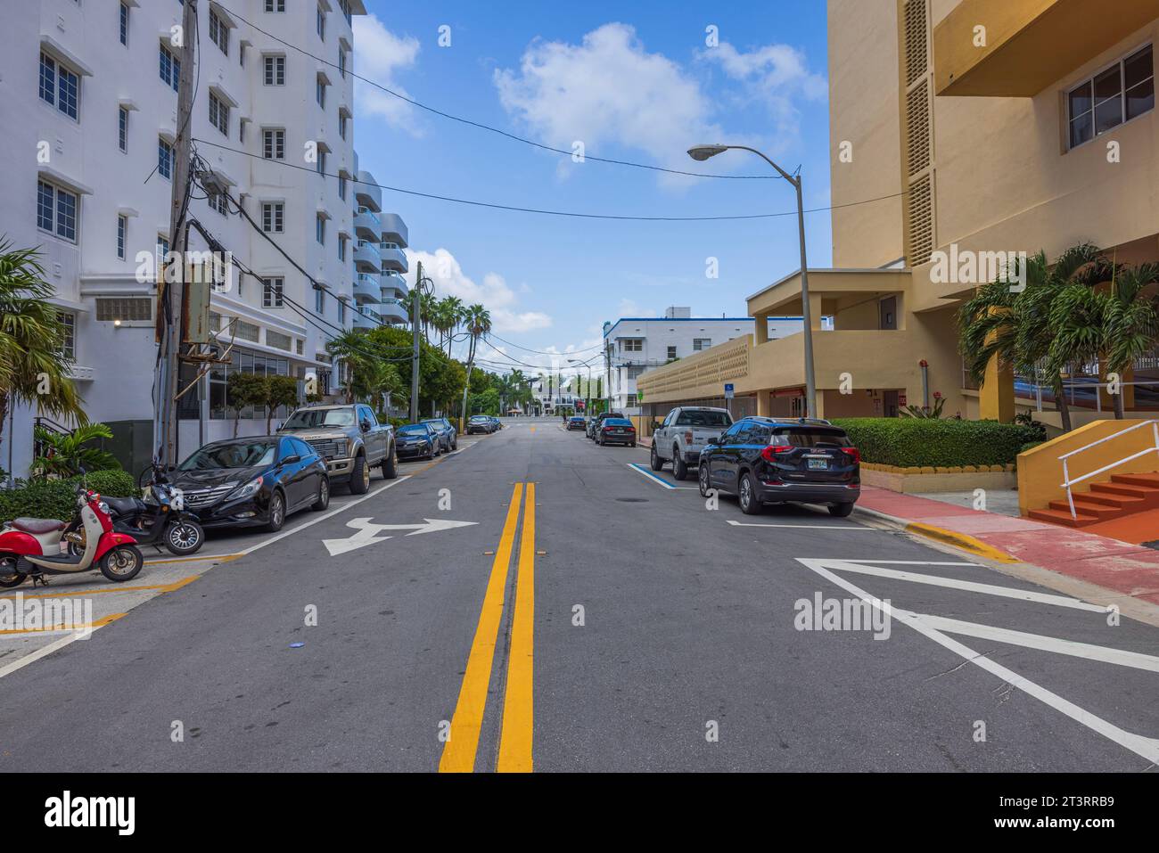 Picturesque cityscape of one of Miami Beach streets with parked cars on both sides, on blue sky with rear white clouds background. Florida, USA. Stock Photo