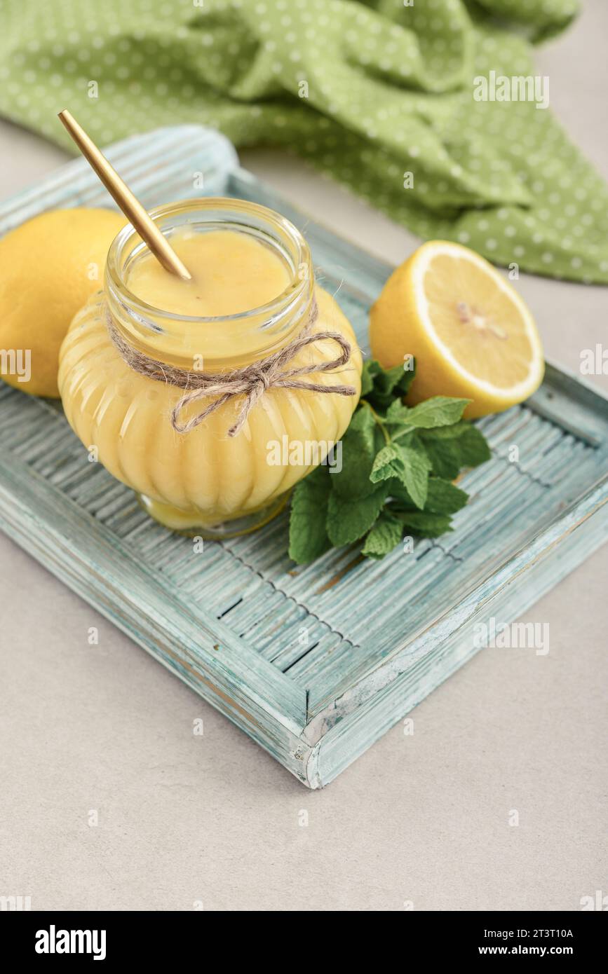 Homemade lemon curd in glass jar with fresh lemons on wooden tray closeup Stock Photo