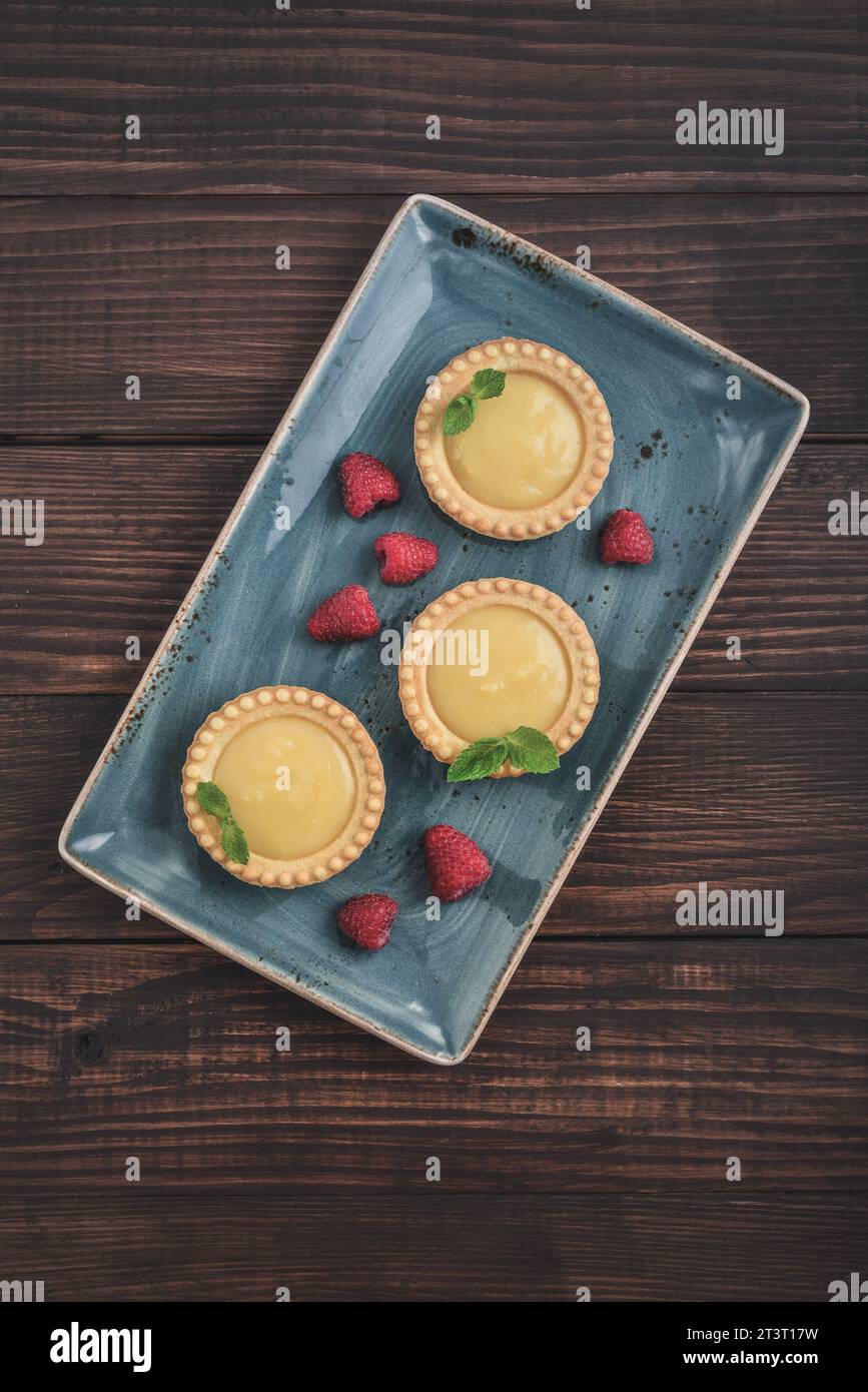 Mini tarts with  lemon, raspberry and custard  filling on wooden rustic board top view Stock Photo