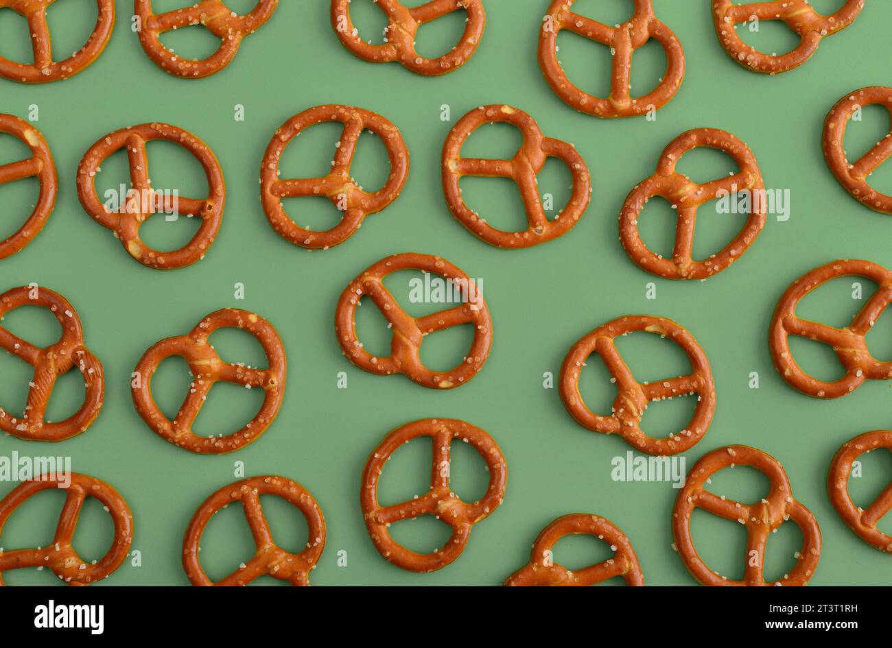 Mini pretzels with sesame seeds as pattern on green background, top view Stock Photo