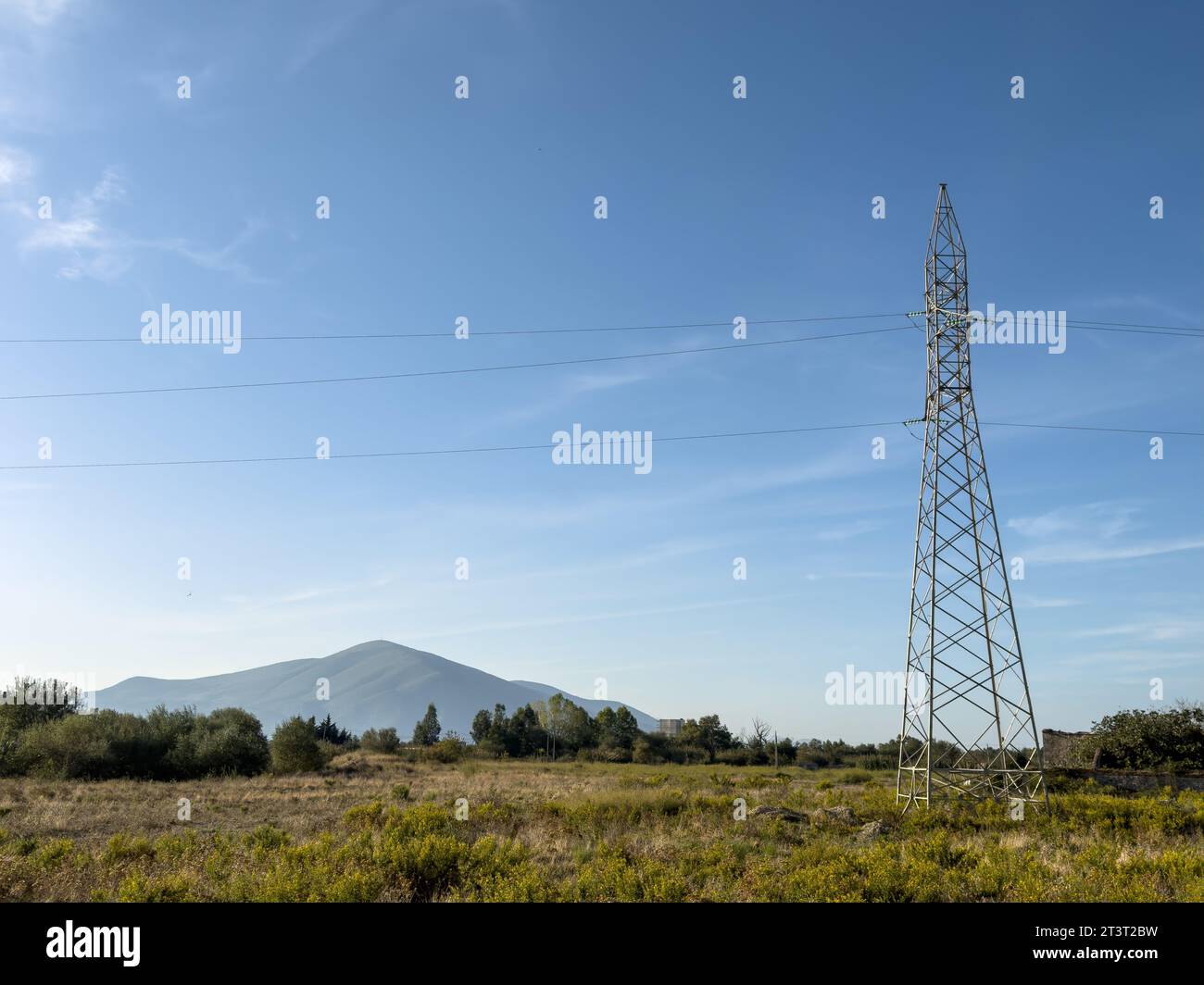 Overhead line pylons, high voltage pylons in meadow with mountains on background at summer sunny day, near Oricum, Albania Stock Photo