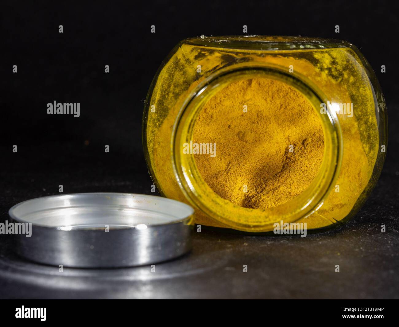 Picture of a jar of turmeric powder on a black background. Turmeric or Curcuma longa, is a flowering plant in the ginger family Zingiberaceae. It is a Stock Photo