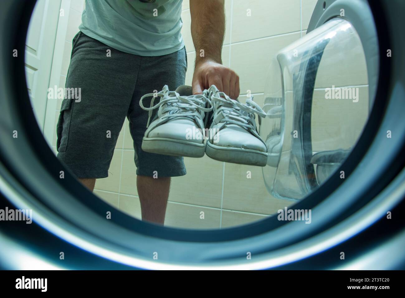 View from inside the washing machine of an unknown person putting dirty and old sneakers into the washing machine for washing Stock Photo