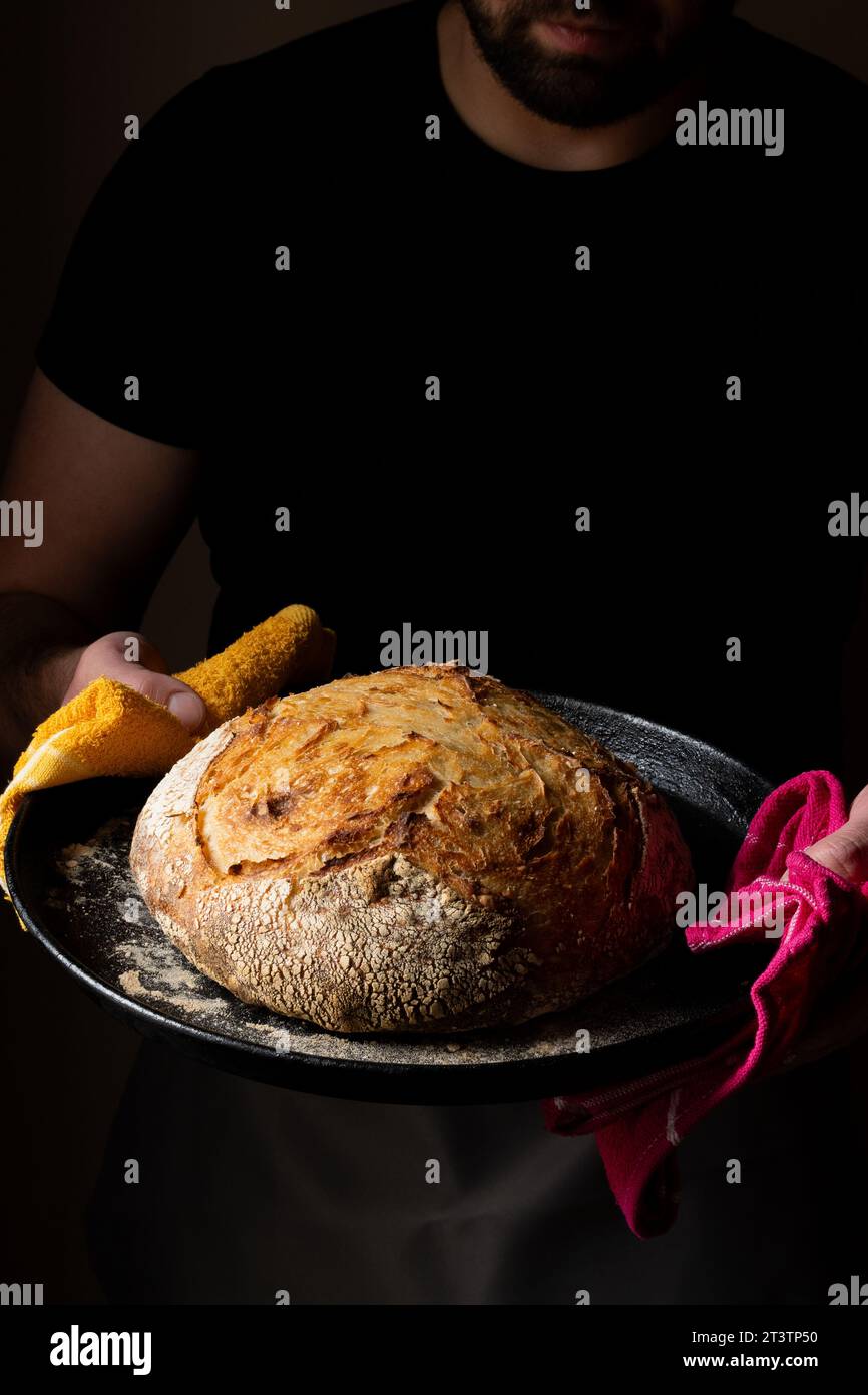 Attractive young Caucasian chef posing with white sourdough bread. The sourdough bread is the central protagonist of the scene, standing out with beau Stock Photo