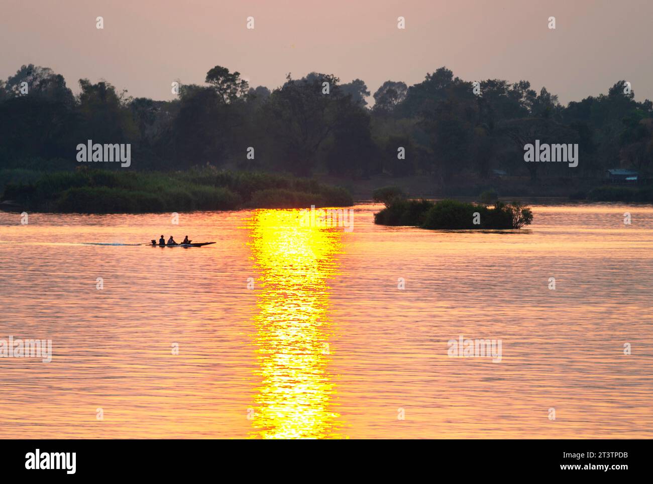 Silhouettes of human figures in a small canoe,drifting across the calm,peaceful waters of the Mekong,through rays of golden light reflected on the wat Stock Photo