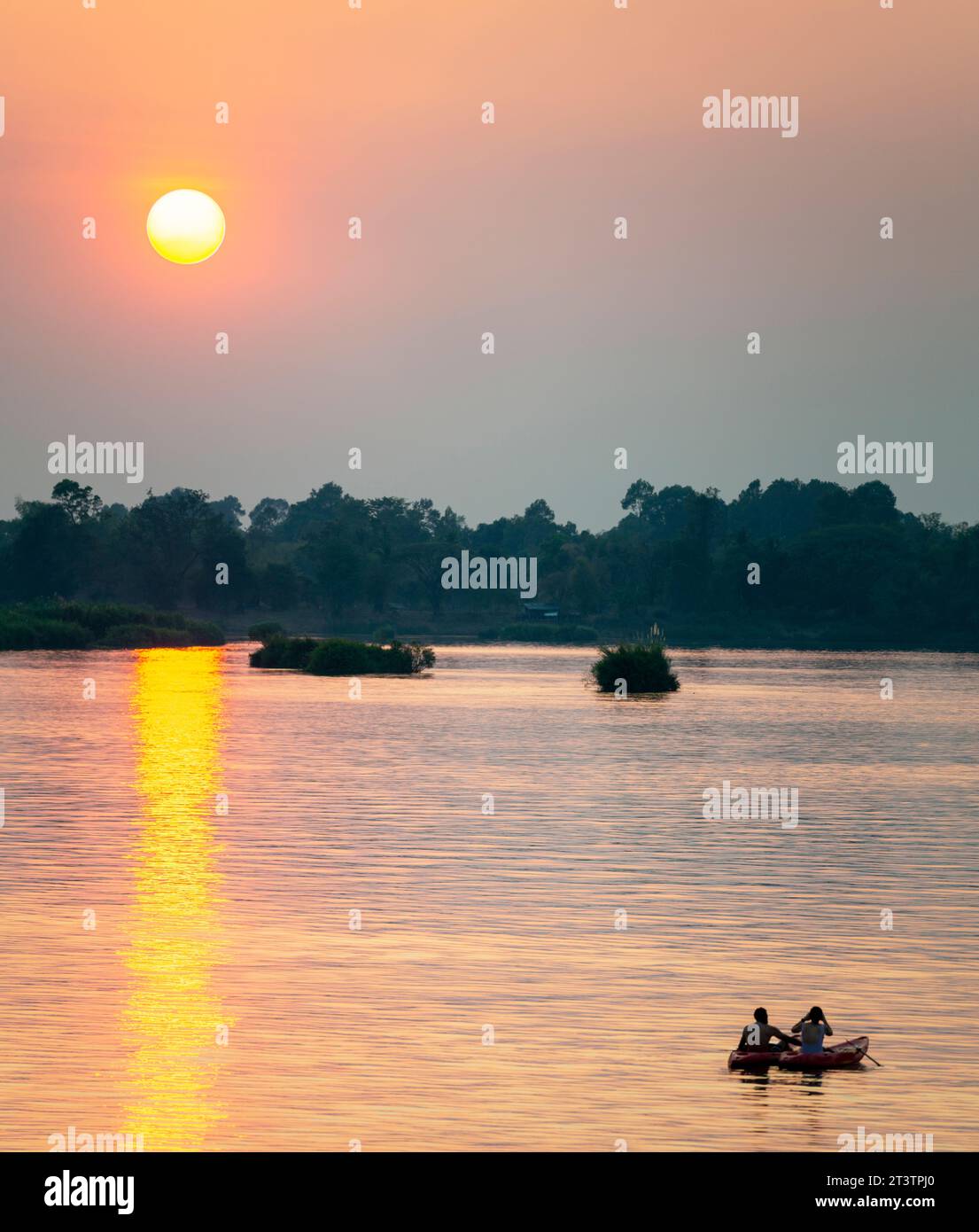 Silhouettes of two human figures in Kayaks,drifting across the calm,peaceful waters of the Mekong,through rays of golden light reflected on the water, Stock Photo