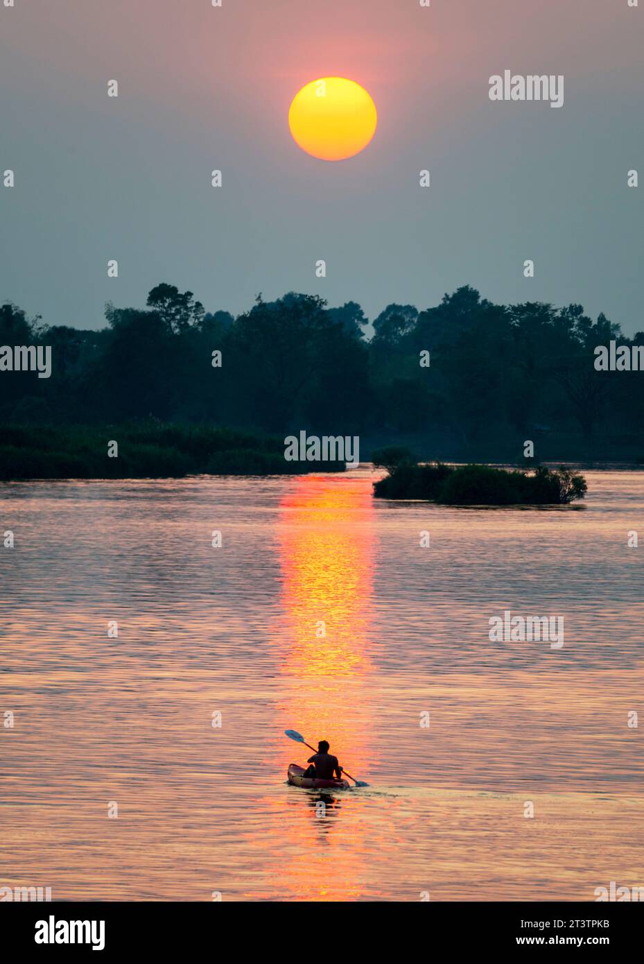 Silhouette of a human figure in a Kayak,drifting across the calm,peaceful waters of the Mekong,through rays of golden light reflected on the water sur Stock Photo