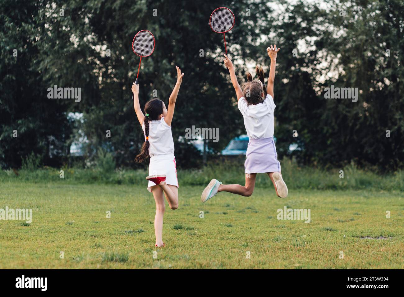 Rear view two girls jumping park holding badminton Stock Photo