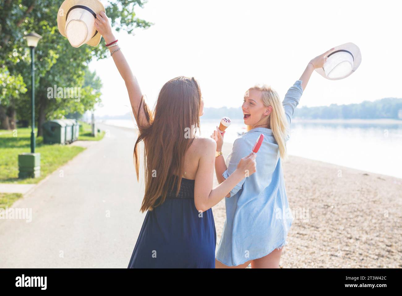 Two young female friend holding hat enjoying icecream beach Stock Photo