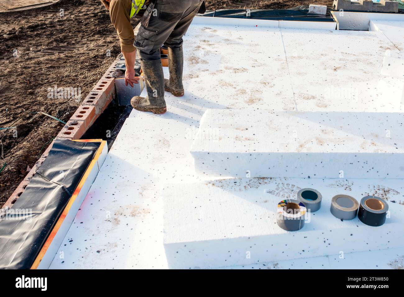Builder placing polystyrene insulation boards on waterproofing membrane