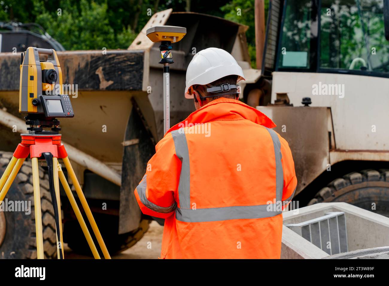 Surveyor site engineer with total positioning station on the construction site of the new road construction with construction machinery and materials Stock Photo