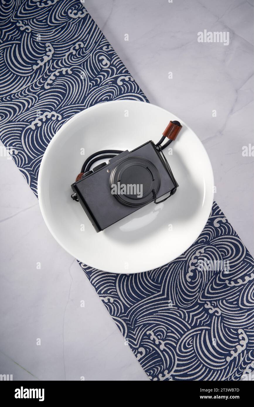 A retro style camera is placed on a white ceramic dinner plate Stock Photo