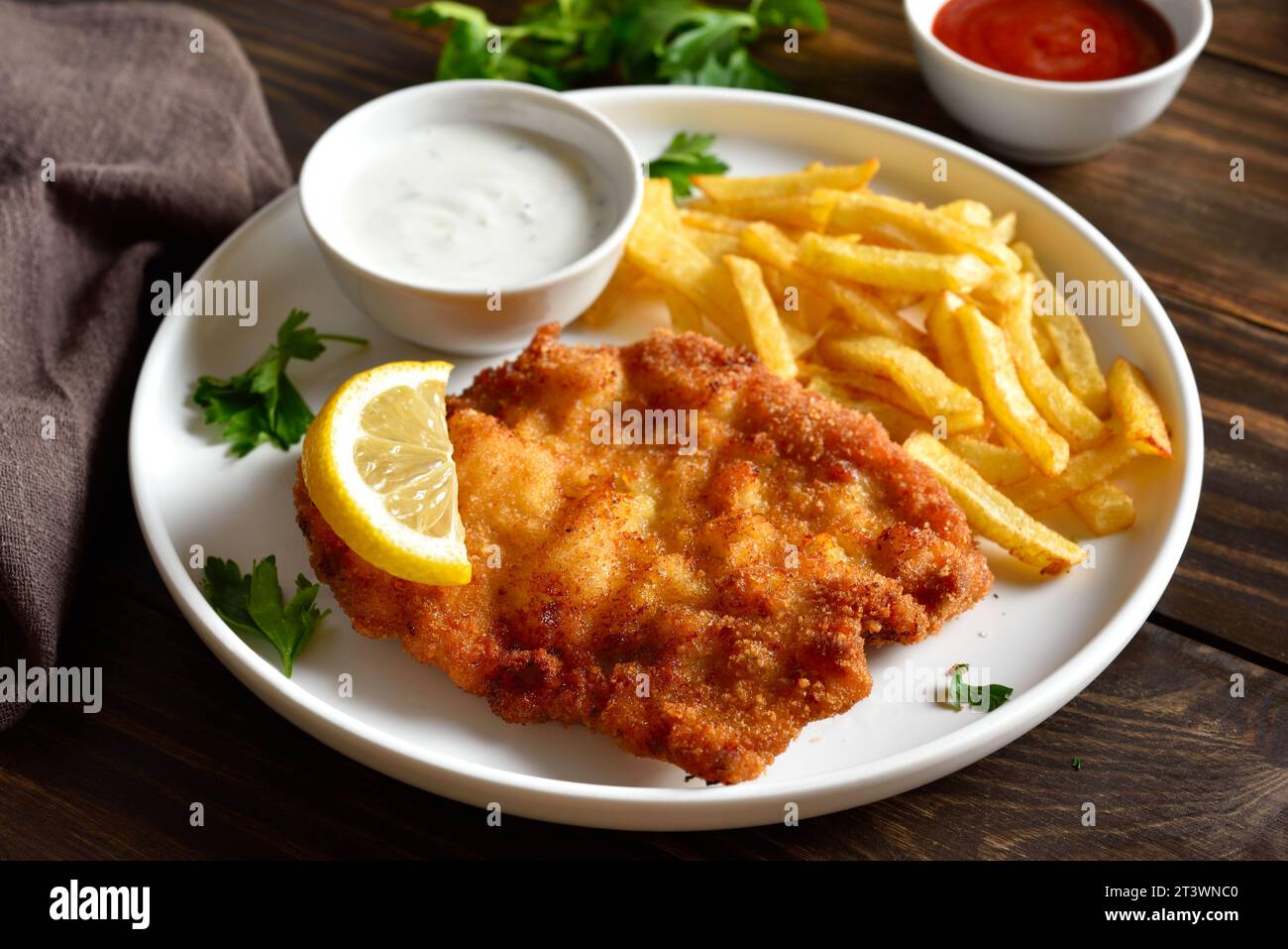 Breaded wiener schnitzel with potato fries and sauce on wooden table. Close up vuew Stock Photo