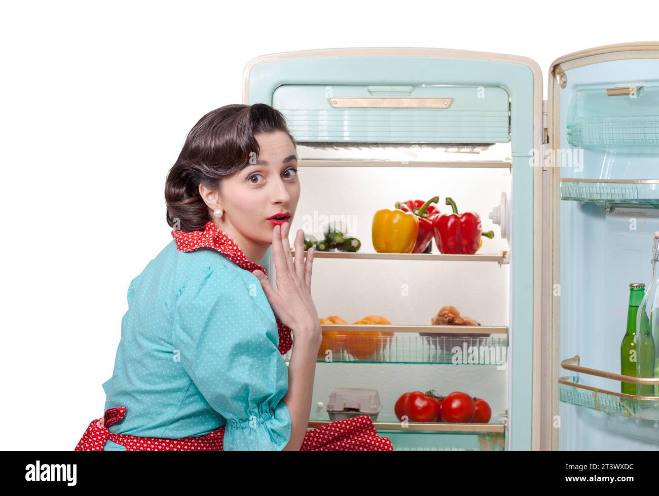Vintage style housewife in the kitchen preparing lunch, she is opening the fridge and looking at camera Stock Photo