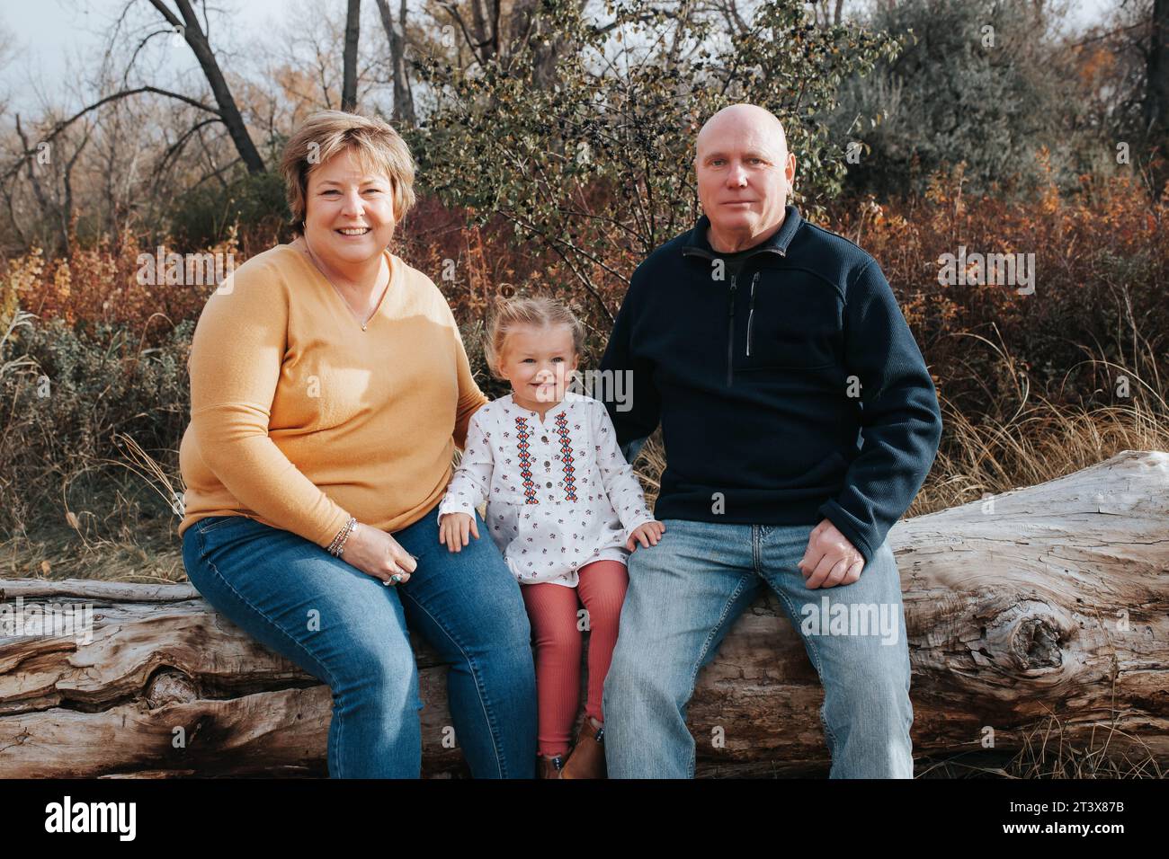 Grandparents and 4-year-old granddaughter on a fall log Stock Photo
