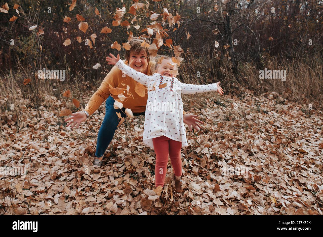 4-year-old and grandma play, tossing fall leaves Stock Photo