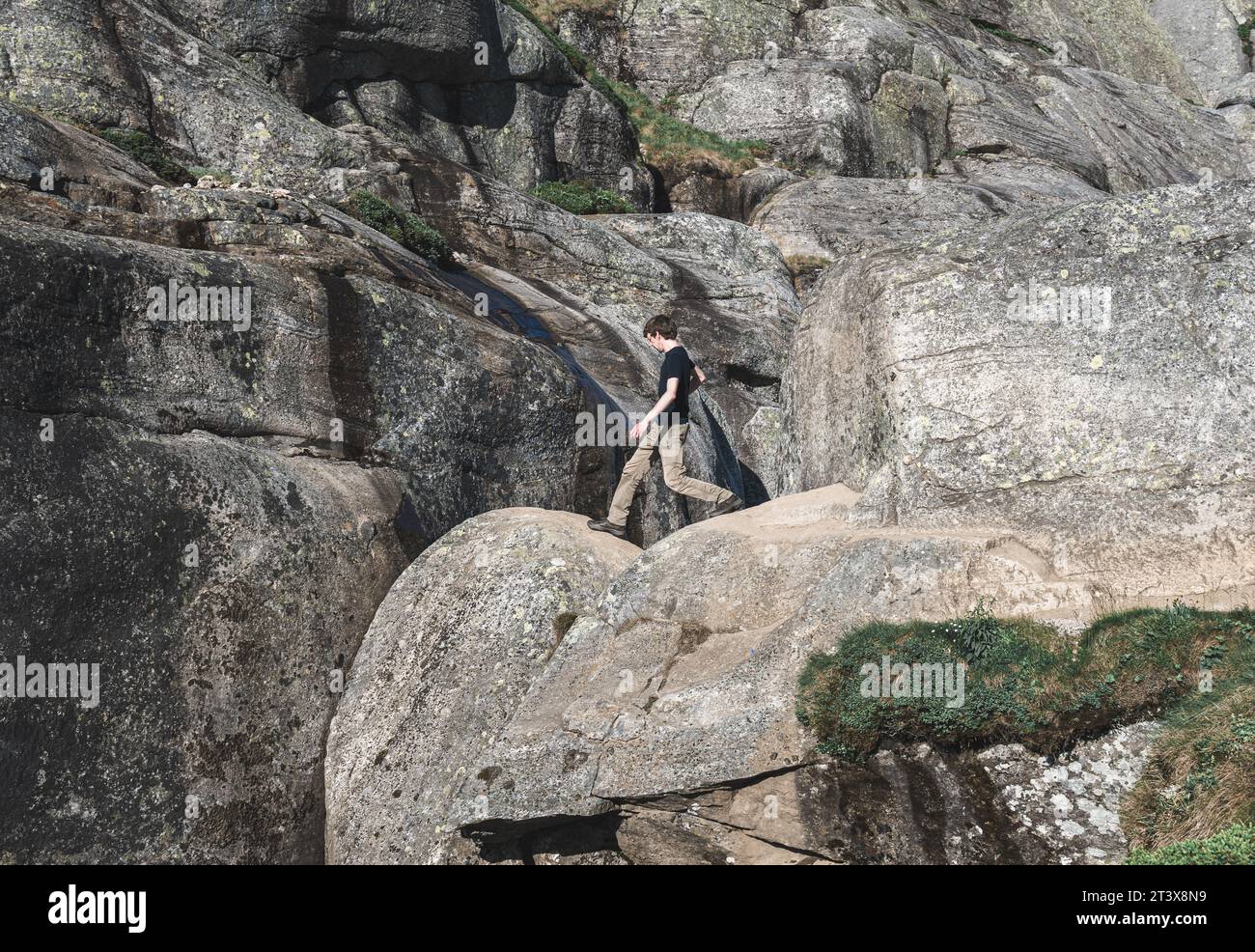 young man climbs a rock Kjerag stuck in a rock in the mountains Stock Photo