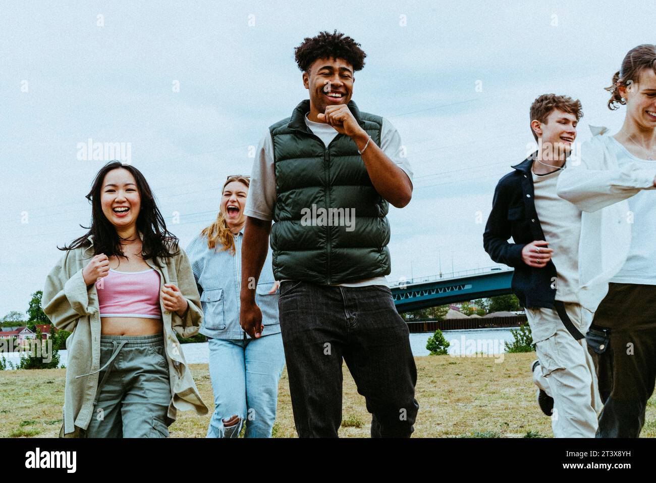 Happy young multiracial friends running against sky Stock Photo