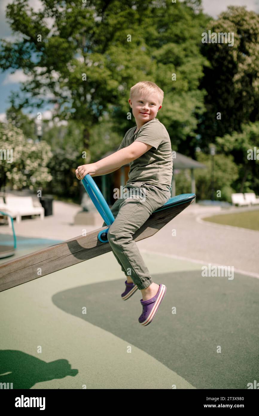 Full length side view of boy with down syndrome enjoying seesaw at park Stock Photo