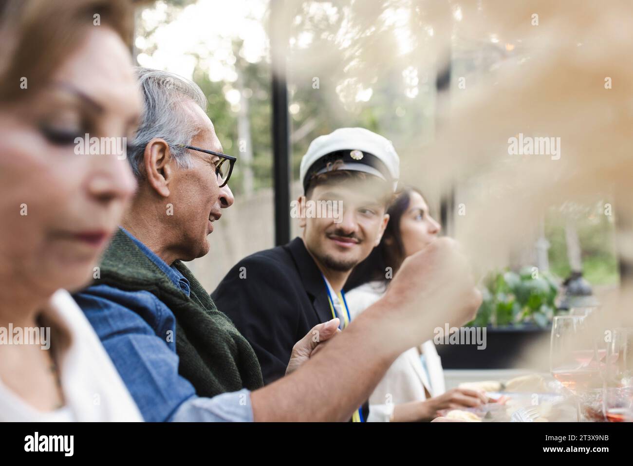Family sitting at dining table while enjoying dinner party in patio