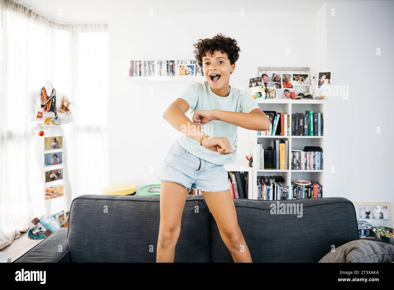 Happy ten years old girl dancing on a sofa in a living room. Girl dancing and having fun while dancing on the sofa of a living room. Stock Photo