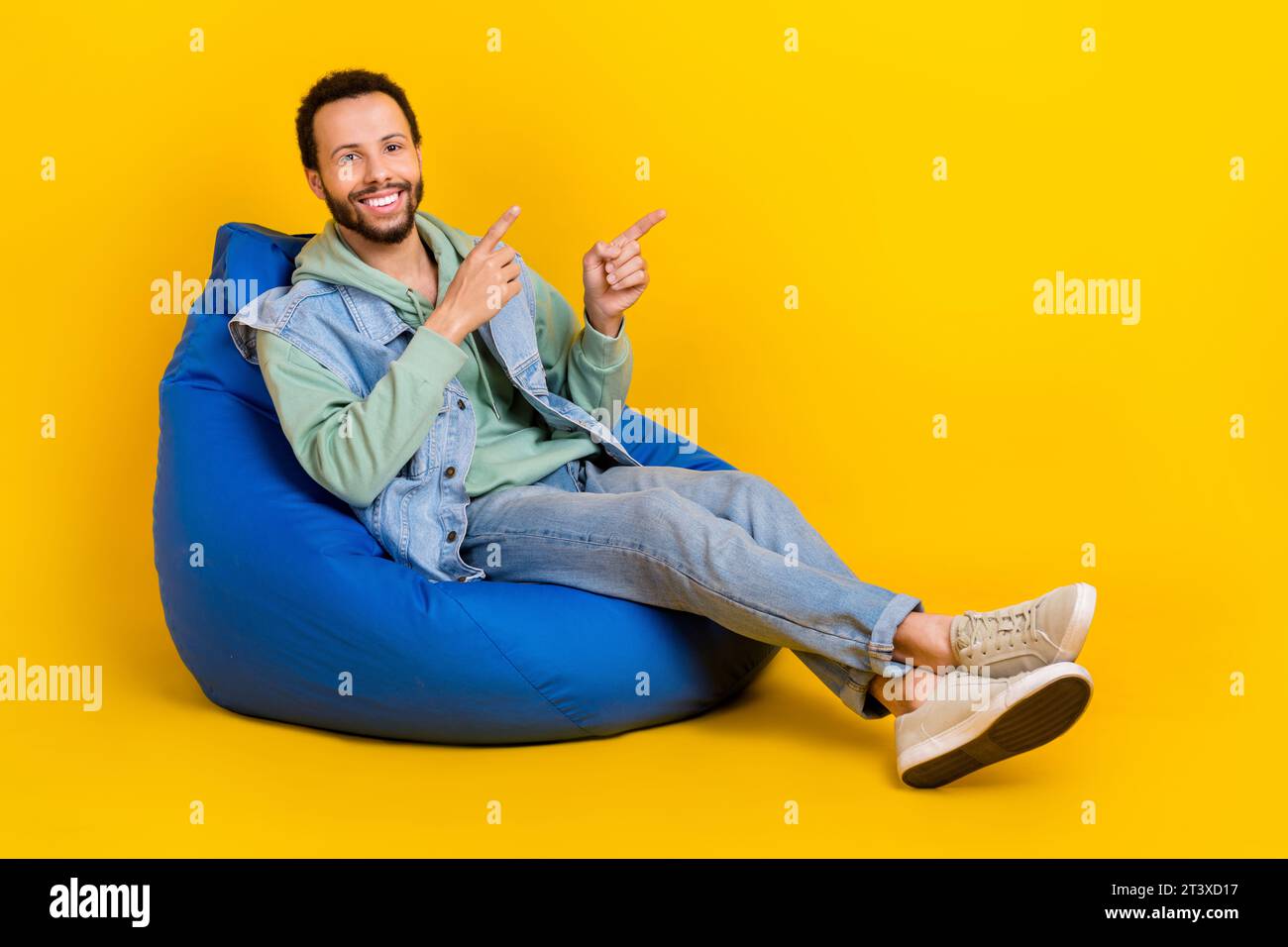 Full body length size cadre of wearing khaki sweatshirt denim waistcoat sit pouf direct fingers novelty isolated on yellow color background Stock Photo