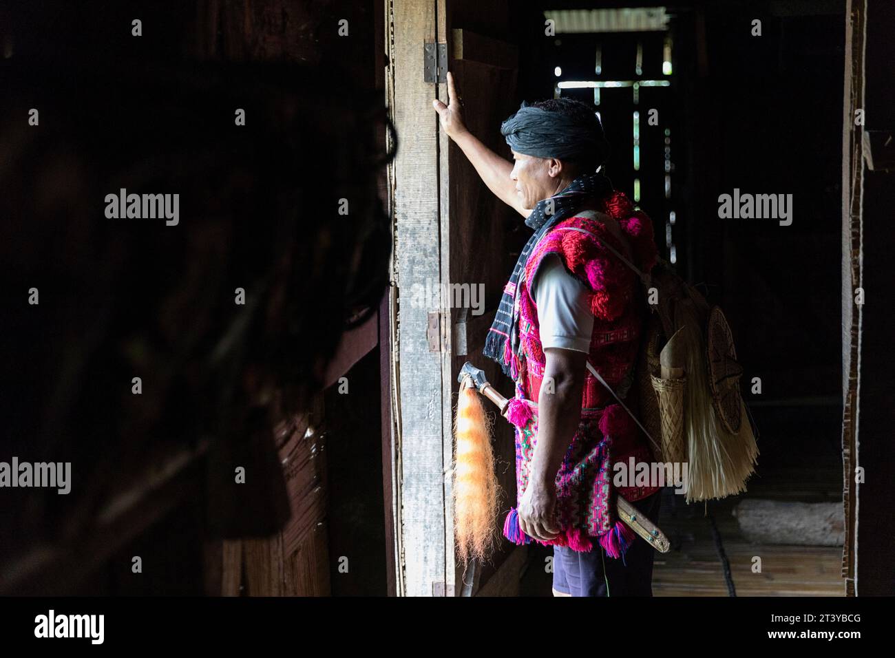 Side view of a man from Adi tribe in traditional clothes standing at the door in traditional wooden house in Assam, Northeast India Stock Photo