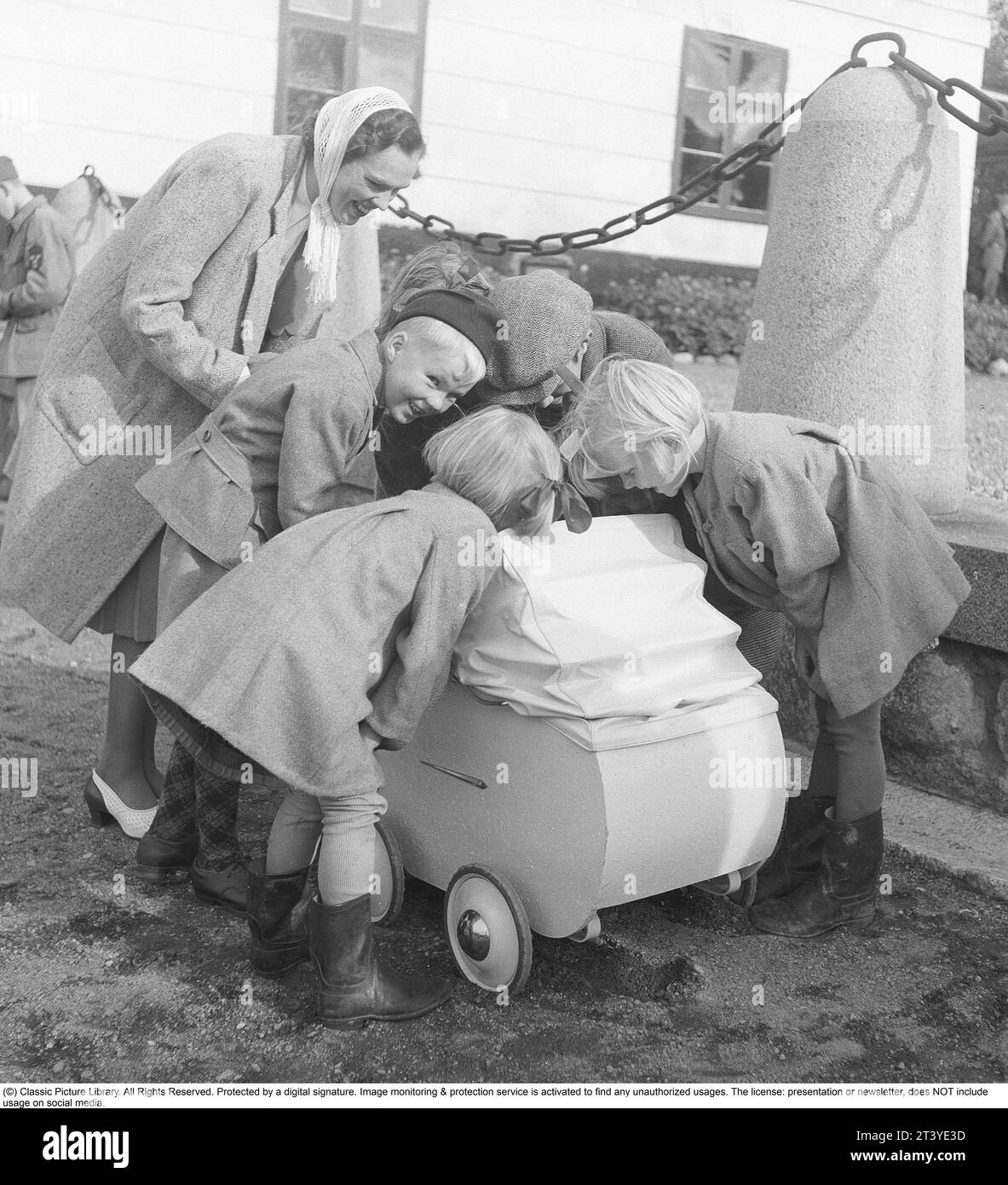 Mother in the 1940s. A young mother is seen with her baby in the carriage, surrounded by curious children who are trying to catch a glimpse of her baby. Sweden 1943. Kristoffersson ref E90-3 Stock Photo