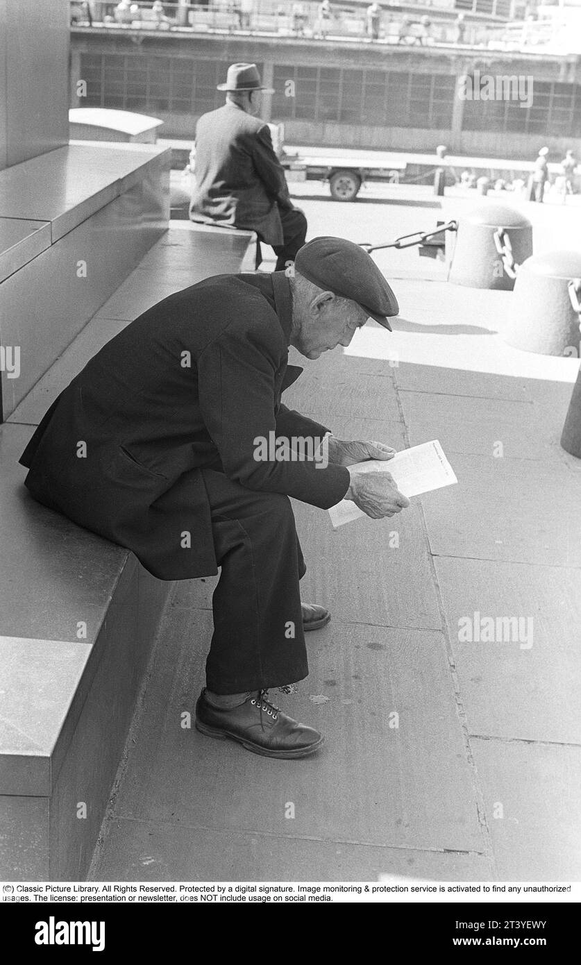 In the 1950s. An elderly man sittting on the steps reading the list of starting horses at the upcoming horseraces on Solvalla horse racing track. He is dressed in a jacket and a cap and looks thoughtful when browsing through the list of starting horses to pick the winner.  Stockholm  Sweden 1953 ref DV1 Stock Photo