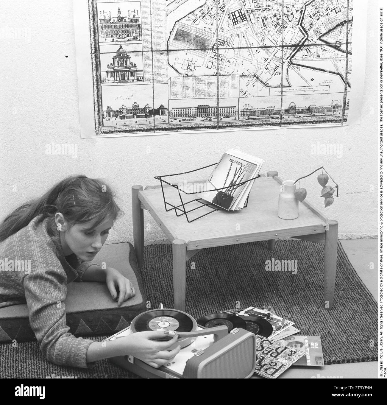 Woman at a gramophone in the 1950s. A typical 1950s teenage girl lying on the floor listening to music from a small gramophone. She is playing the type of records called singles. A record that typically contained a recording of fewer tracks than an LP record. This single record was played at the speed 45 rpm (revolutions per minute) and was 7 inches in diameter, 17,8 cm. The first single record was released 31 march 1949 by RCA Victor. Sweden 1959. Ref SSMSAX000521L Stock Photo
