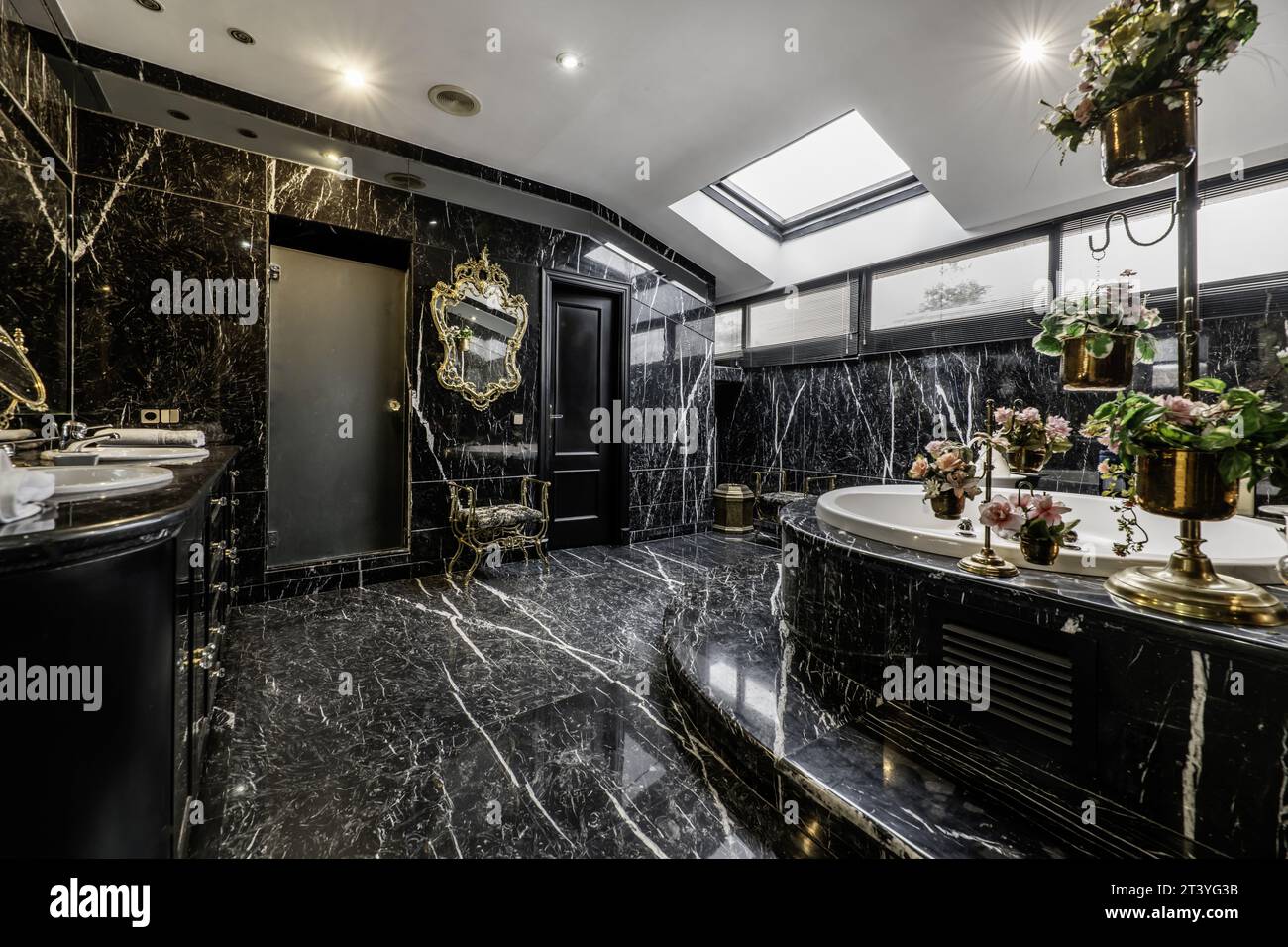 Large bathroom with a circular whirlpool bathtub, all tiled with black marble floors Stock Photo