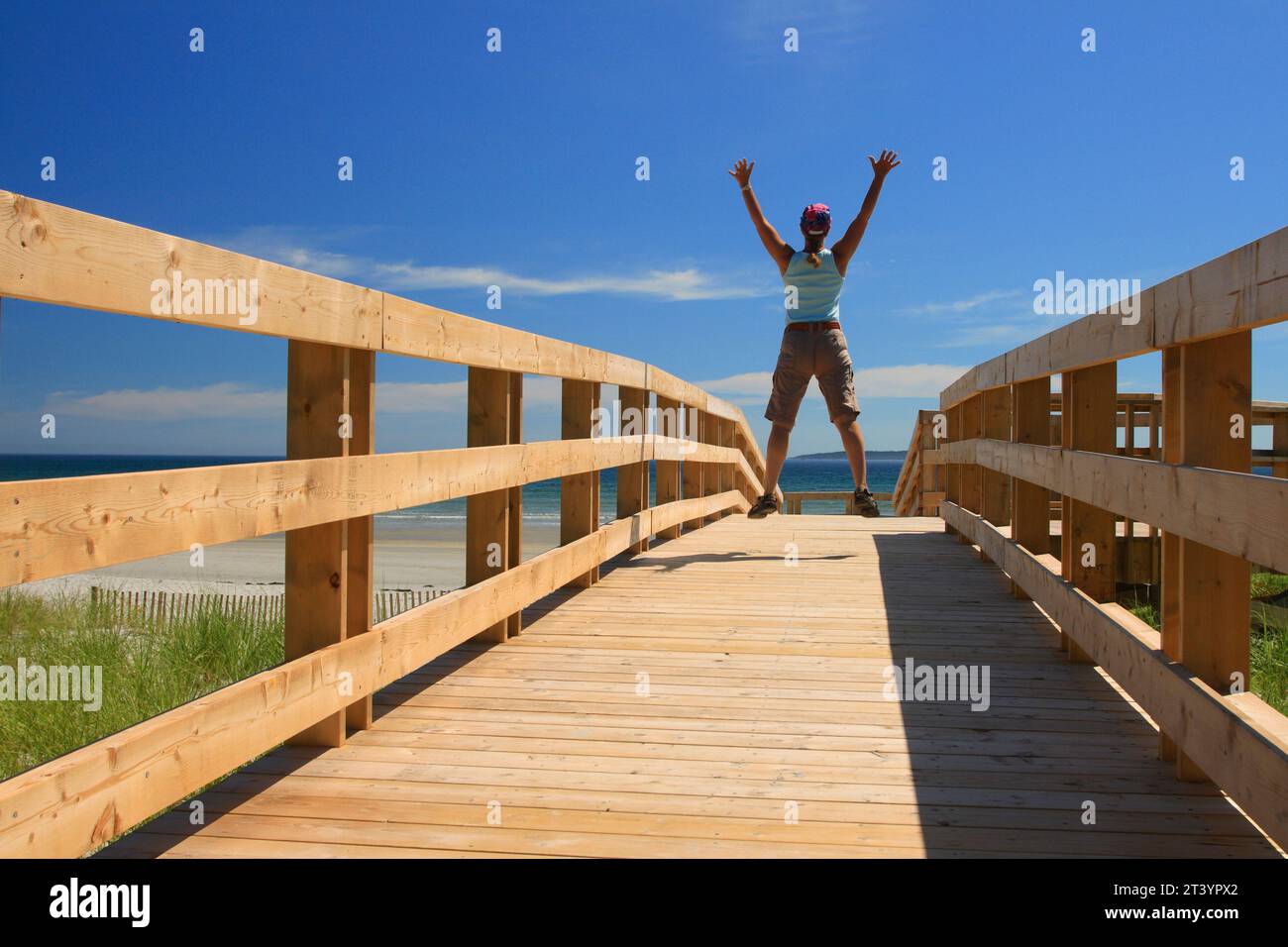 a woman jumping with glee or joy on a boardwalk at the beach Stock Photo