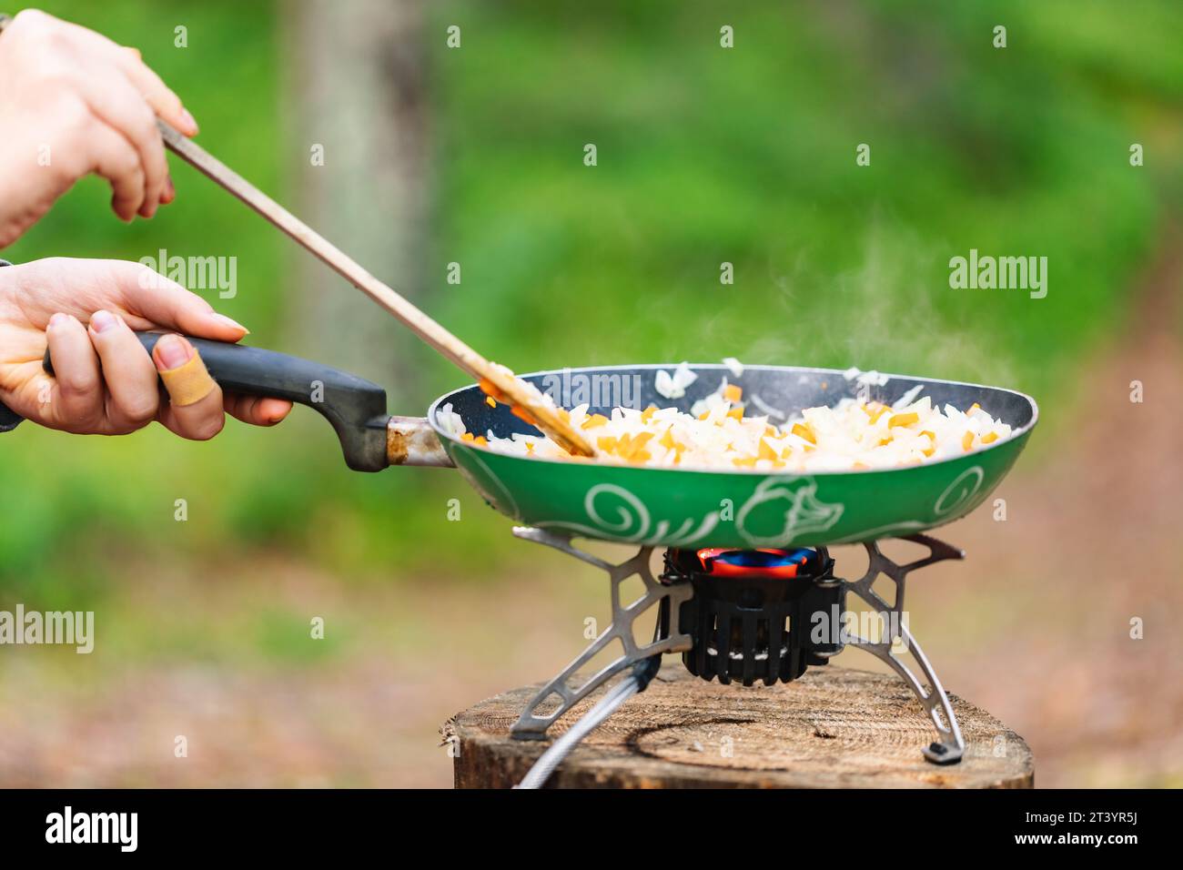 Cooking meal in a pan on a portable stove during wild camping in a forest Stock Photo