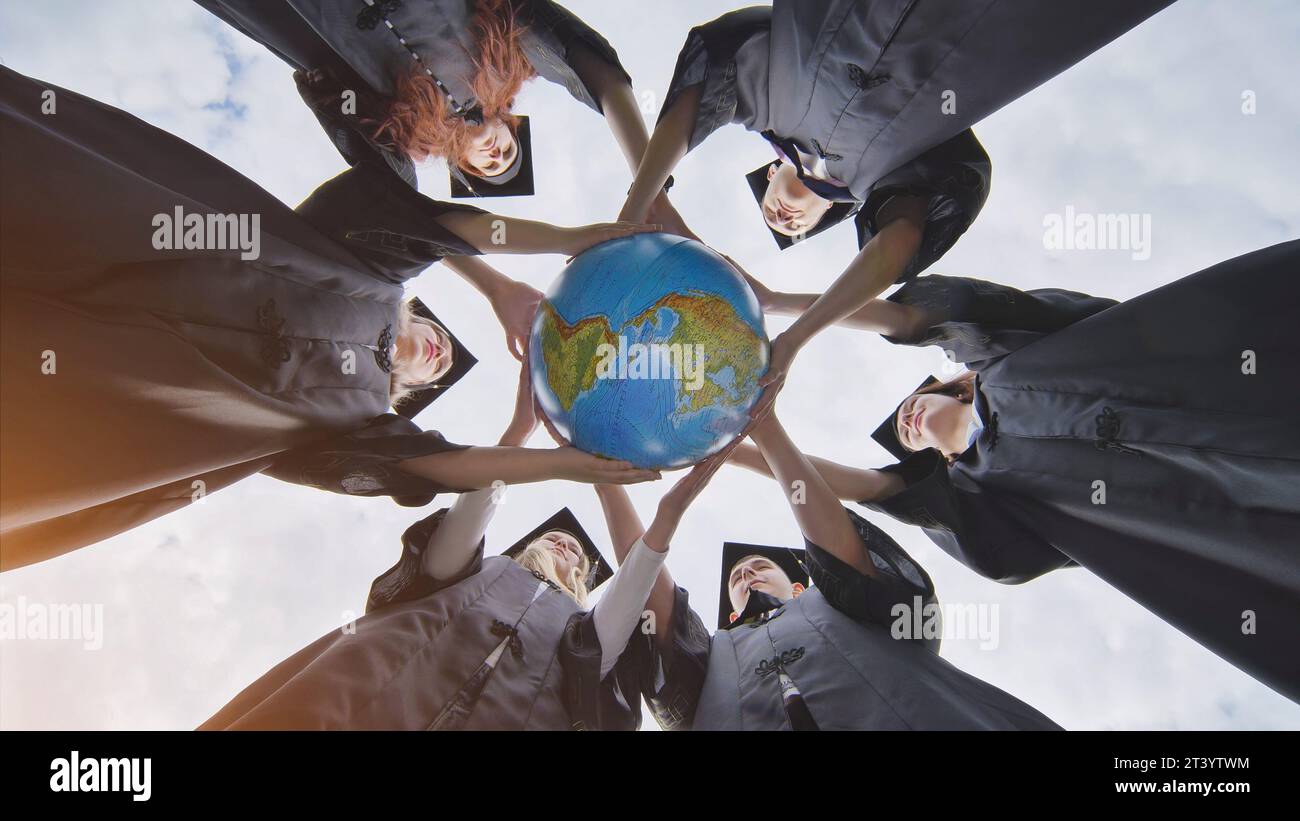 Graduating students hug and toss a geographical globe of the world overlooking north and south america. Stock Photo