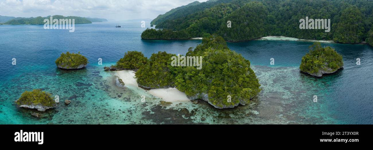 Scenic limestone islands, covered by tropical vegetation, are fringed by diverse coral reefs in the calm Alyui Bay, Raja Ampat, Indonesia. Stock Photo