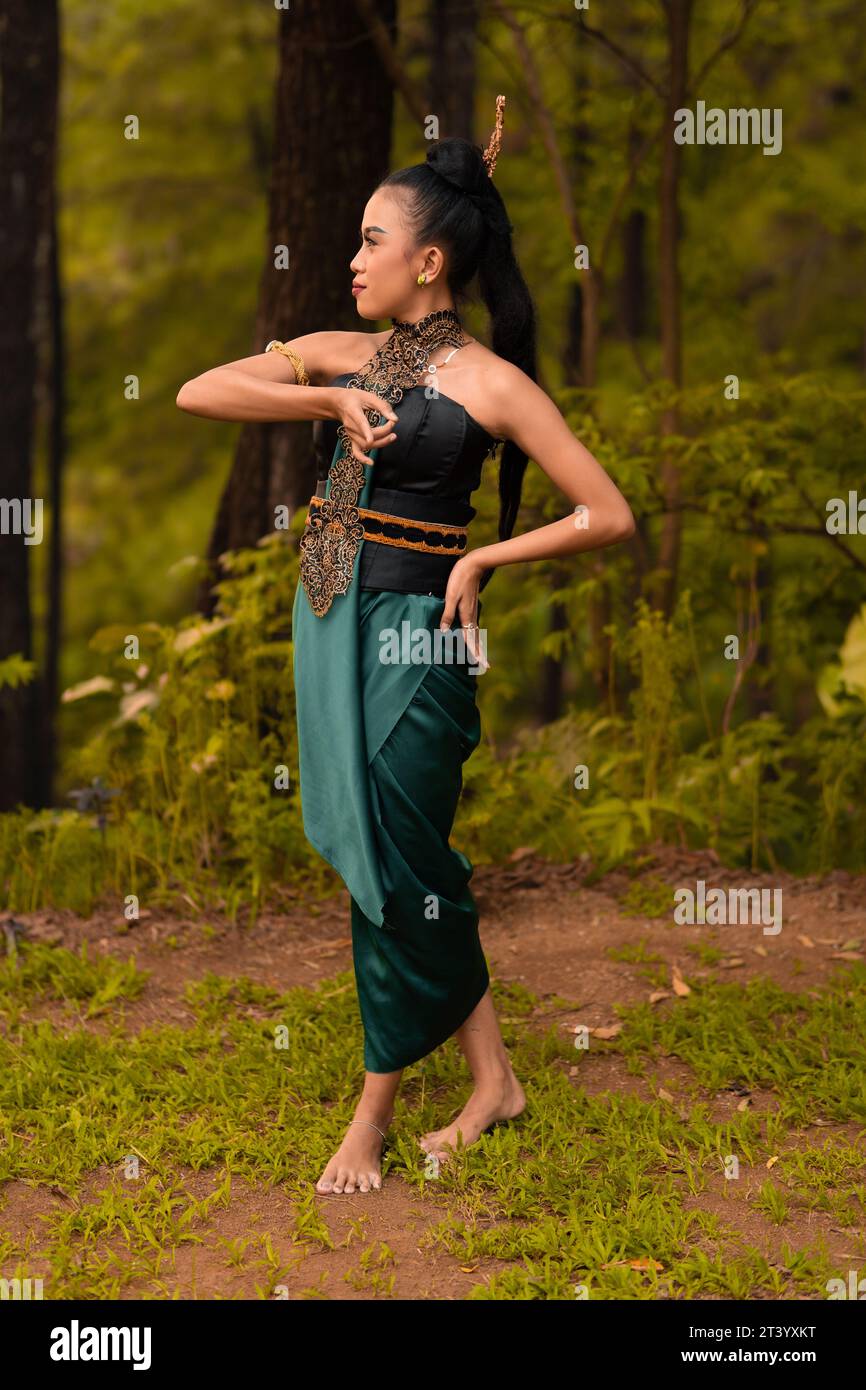 Beautiful Indonesian dancers with traditional green costumes and black tied hair posing inside the forest after performing Stock Photo