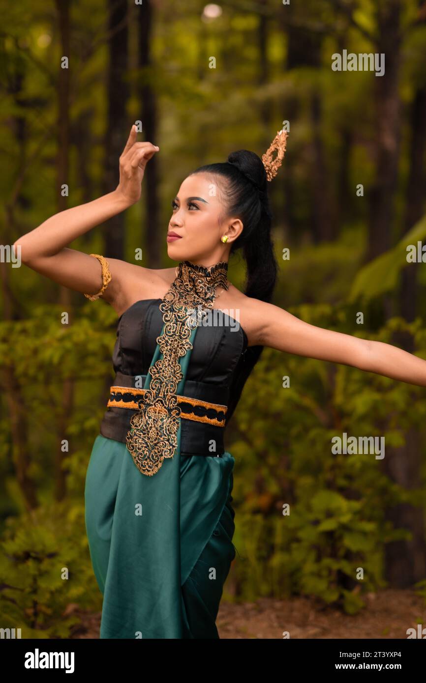 Beautiful Indonesian dancers with traditional green costumes and black tied hair posing inside the forest after performing Stock Photo