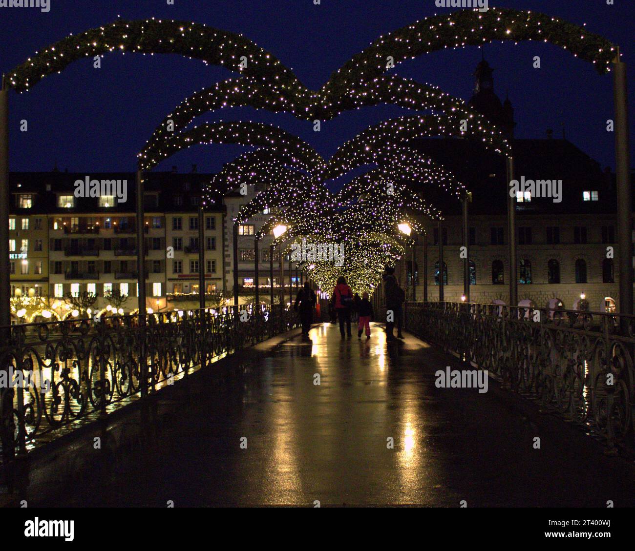 Rathaussteg bridge in Luzern, Switzerland. Seen at Christmas time covered in wreaths and fairy lights. People crossing a lit xmas bridge at night Stock Photo