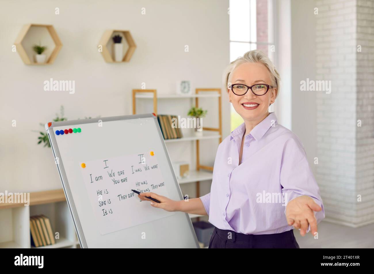 Happy online English teacher standing by white board and explaining grammar rules Stock Photo