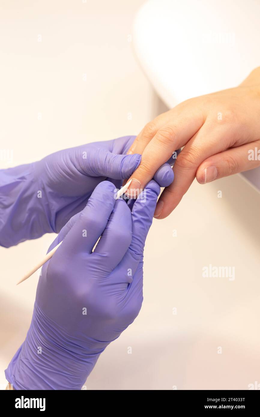 Manicure technician pushes back client cuticles, holding wooden cuticle