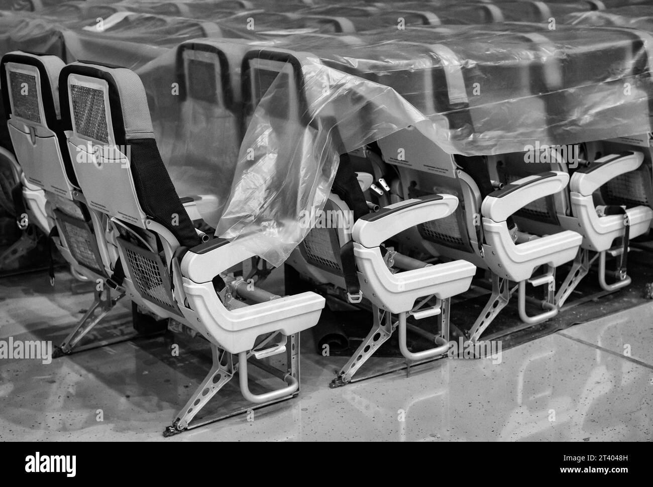 Photo of the disassembled airplane seats in the hangar, covered with protective foil. Black and white photo. Stock Photo