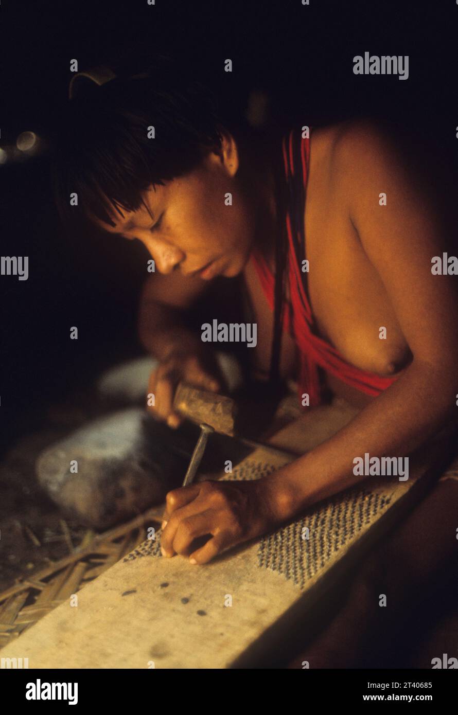 Piaroa (endonym: Wothiha, Wo’tiheh, Wotuha) indigenous woman inserting small stones on board to make manioc (cassava) grater. Guiana Highlands, Venezuela, South America. The Wothiha are one of the largest ethnic groups of Venezuela, numbering about 14,000. They speak a Salivan language. Part of their territory has been invaded by illegal miners and Colombian guerillas. This picture shows a craft no longer practiced by the Wothiha, as, according to anthropologist Stanford Zent who studied them 15 years later they now use mechanized manioc graters Stock Photo
