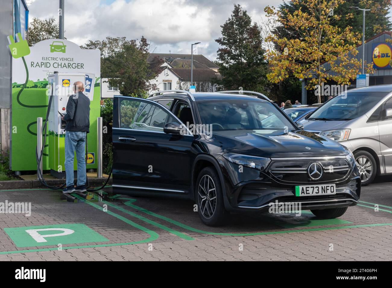 Man charging his car battery at an electric vehicle rapid charger in a Lidl supermarket car park, England, UK Stock Photo