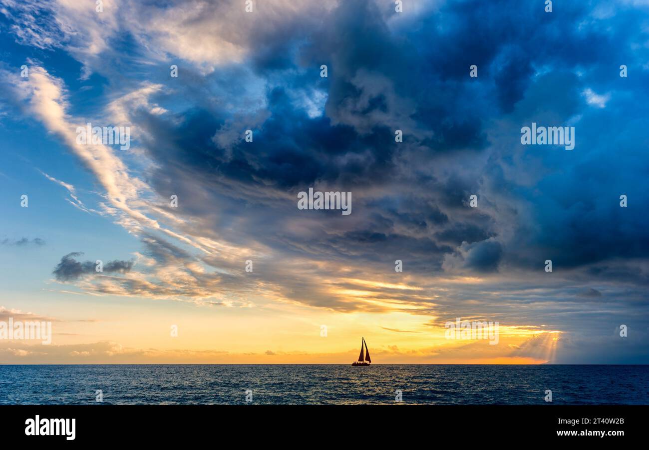 A Sailboat Is Approaching A Dark Looming Ocean Storm With Sun Rays Breaking Through Stock Photo