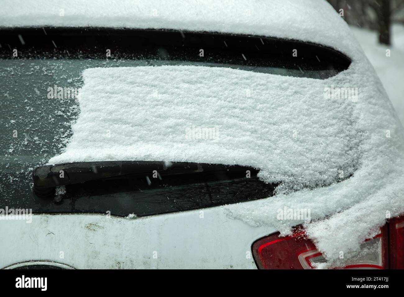 rear car window covered with a layer of snow blocked windshield wiper with snowdrift dirty rear tailgate, nobody. Stock Photo