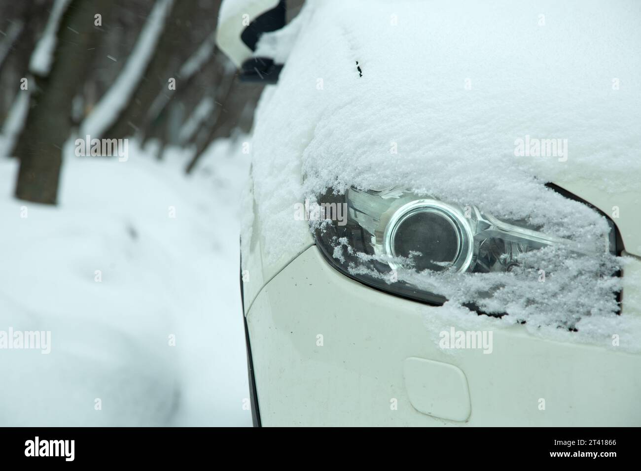 car headlight with lens xenon light covered with snow in winter weather, snowdrifts on the road. close-up of a vehicle detail. Stock Photo